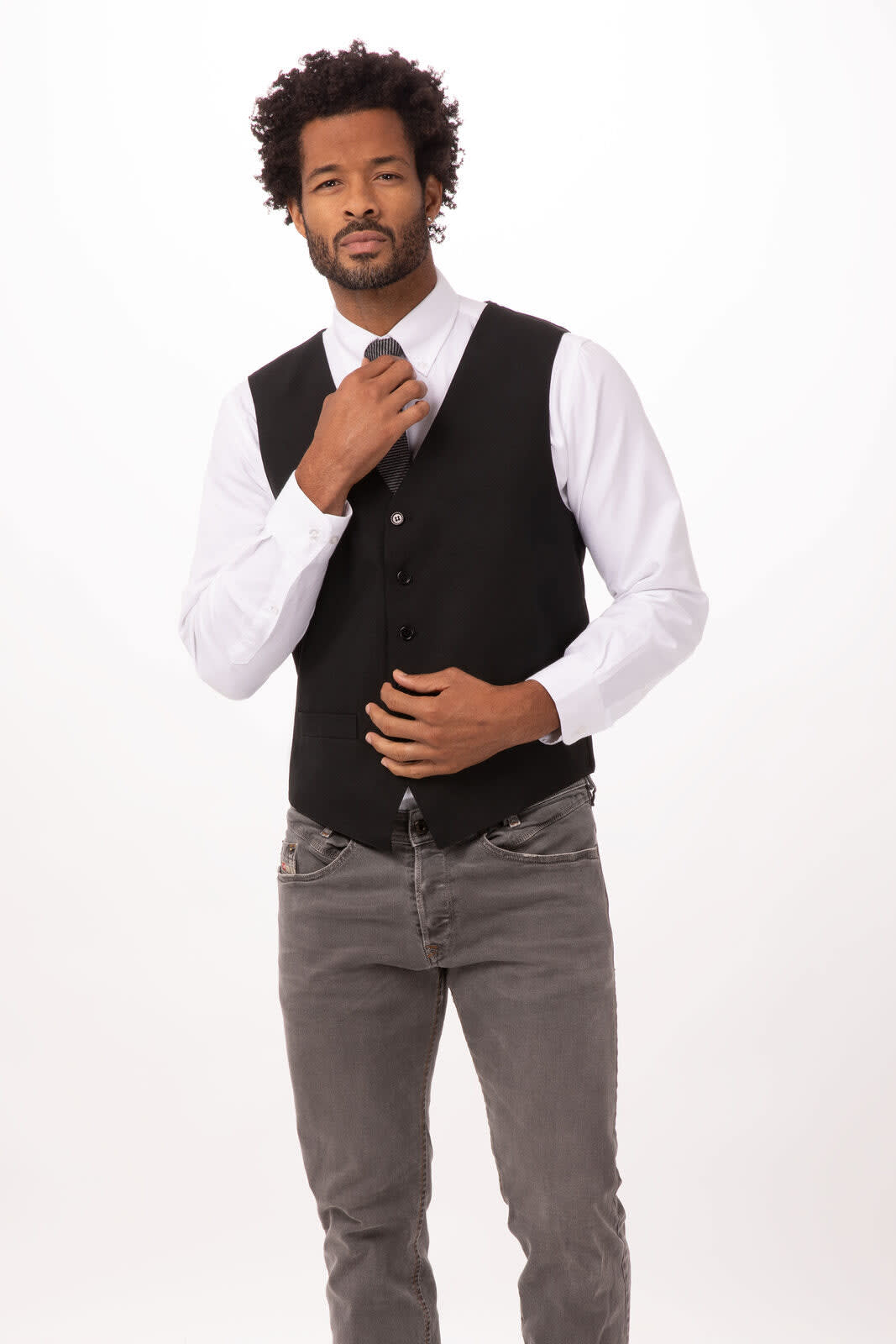 A man wearing a black essential vest over a white shirt, paired with grey jeans. The vest features buttons and a logo.