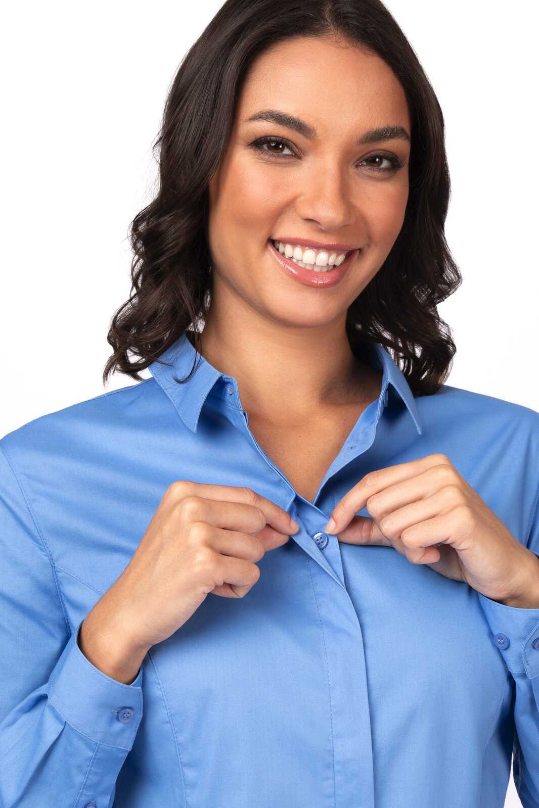 A woman smiling while adjusting a button on a light blue formal women's dress shirt. The shirt features a collar and long sleeves.