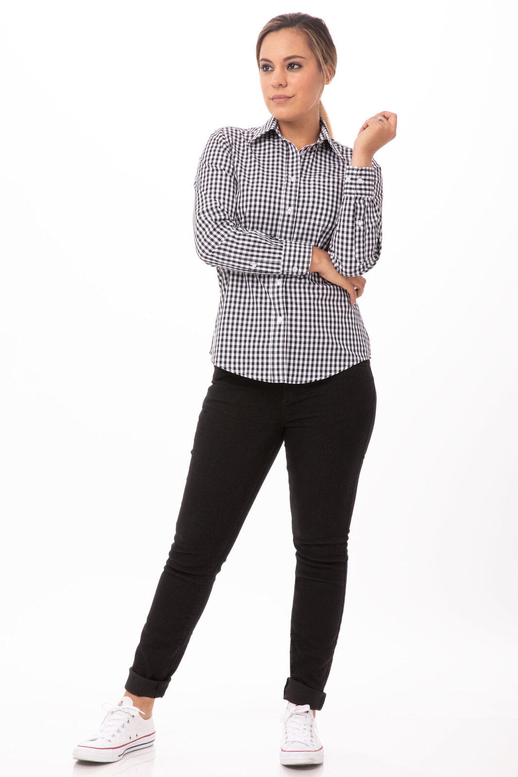 A woman poses in a black and white gingham button-up shirt paired with black pants and white sneakers.