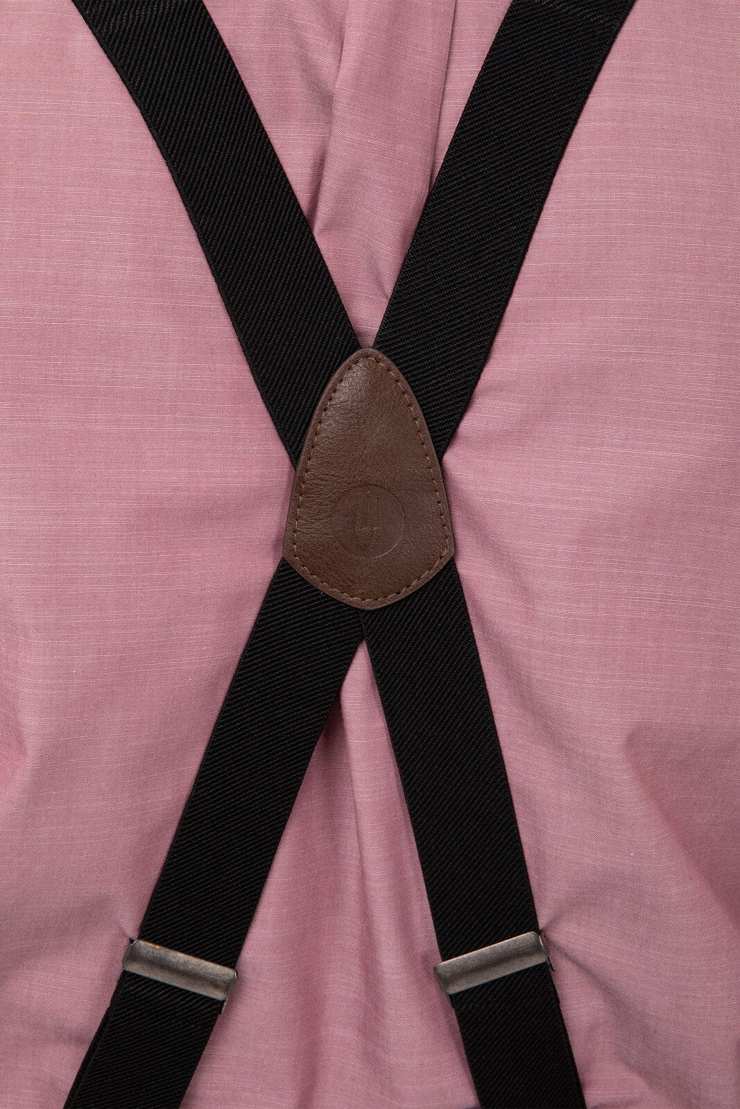 A pair of pink pant suspenders featuring black straps and a brown leather patch in the centre.