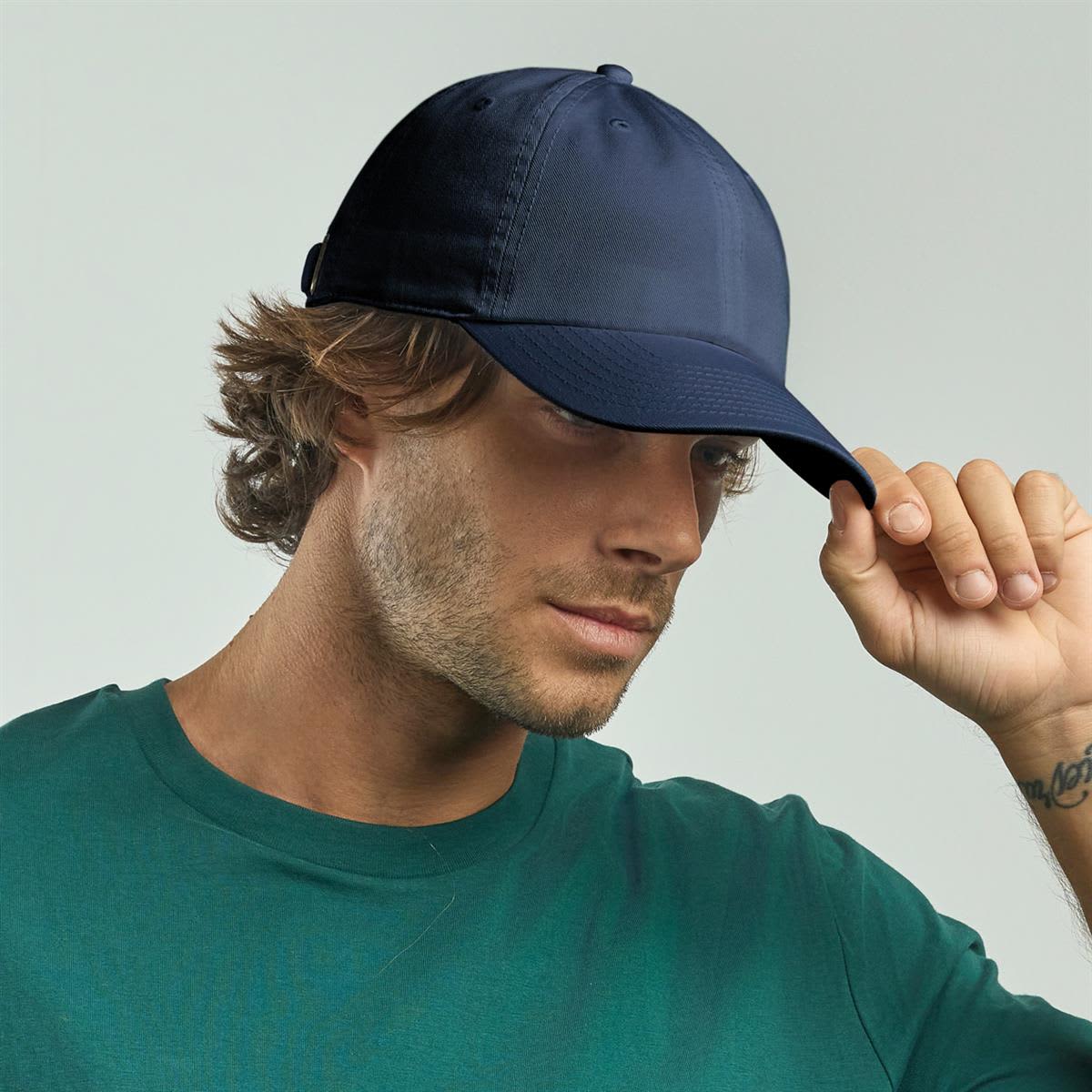 Fraser Organic Dad Hat LE-A5700 A navy organic dad hat is worn by a man with wavy hair, paired with a green shirt. The hat features a logo.