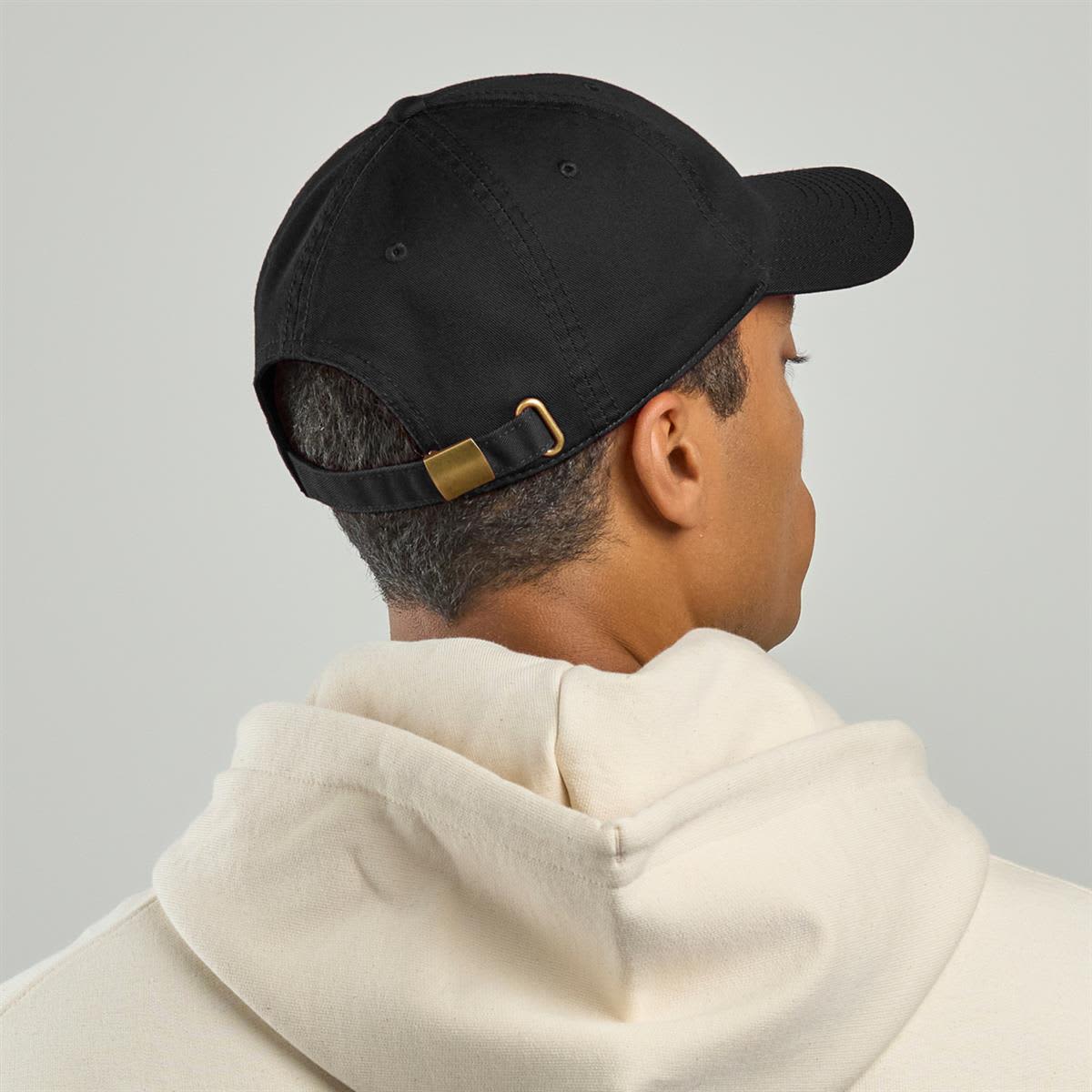 Fraser Organic Dad Hat LE-A5700 A black organic dad hat with an adjustable strap, worn backward by a person in a light-coloured hoodie.