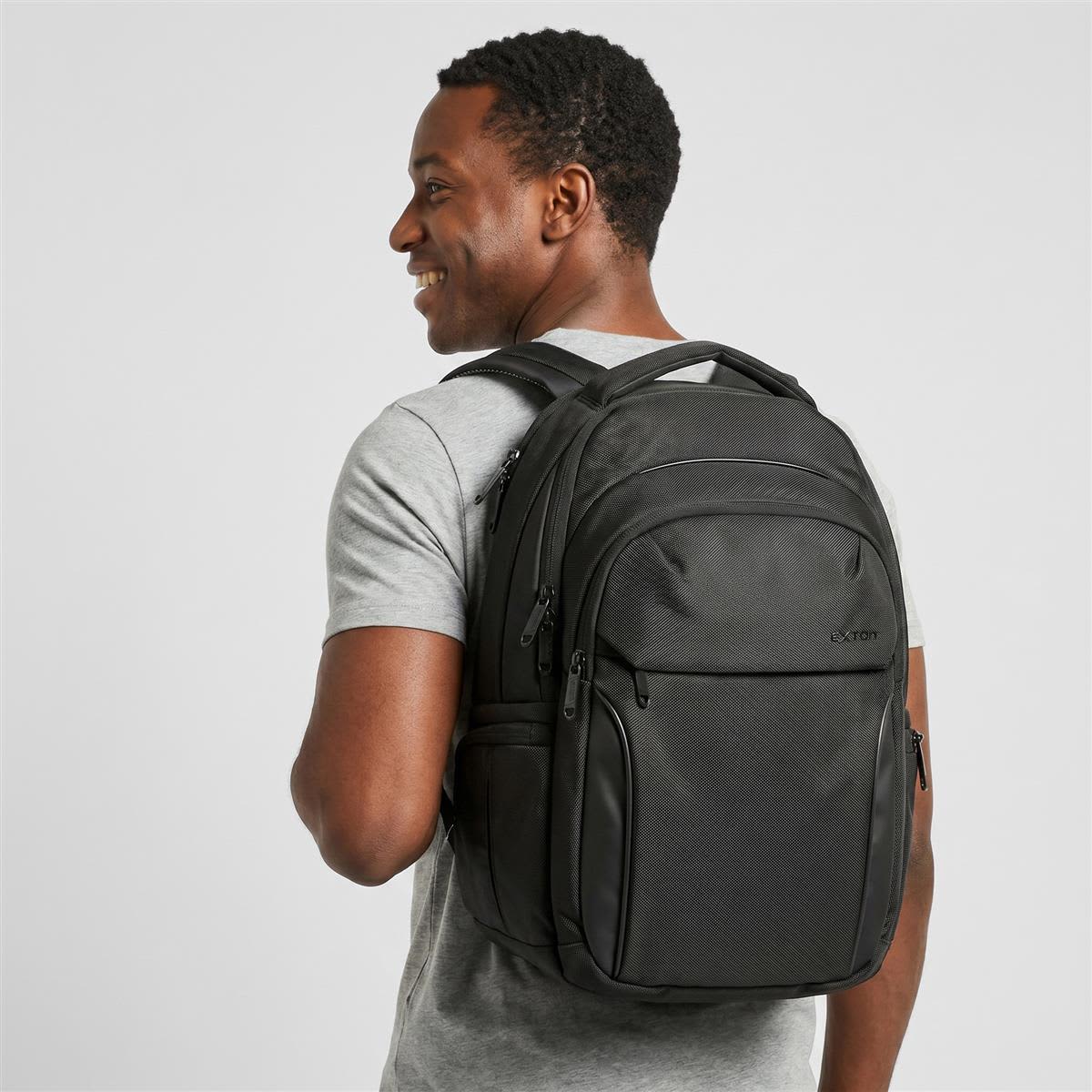 A man wearing a black Exton laptop backpack, featuring multiple compartments and a logo.