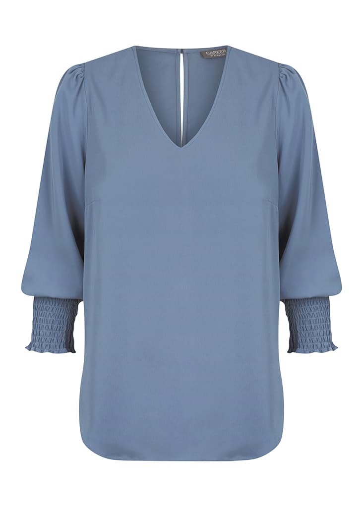 A blue Cleo V Neck shirt with long, puffed sleeves and smocked cuffs. It features a deep V-neckline and branding.