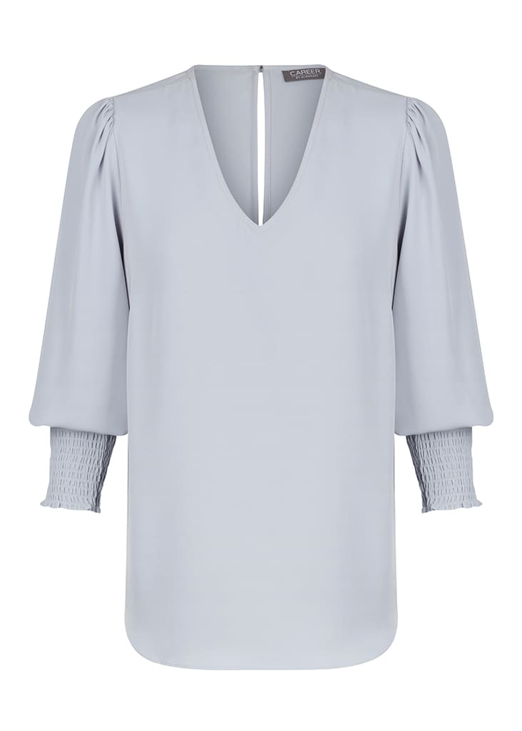 A light blue V-neck shirt with puffed sleeves and smocked cuffs, featuring a back slit detail. It has a logo.