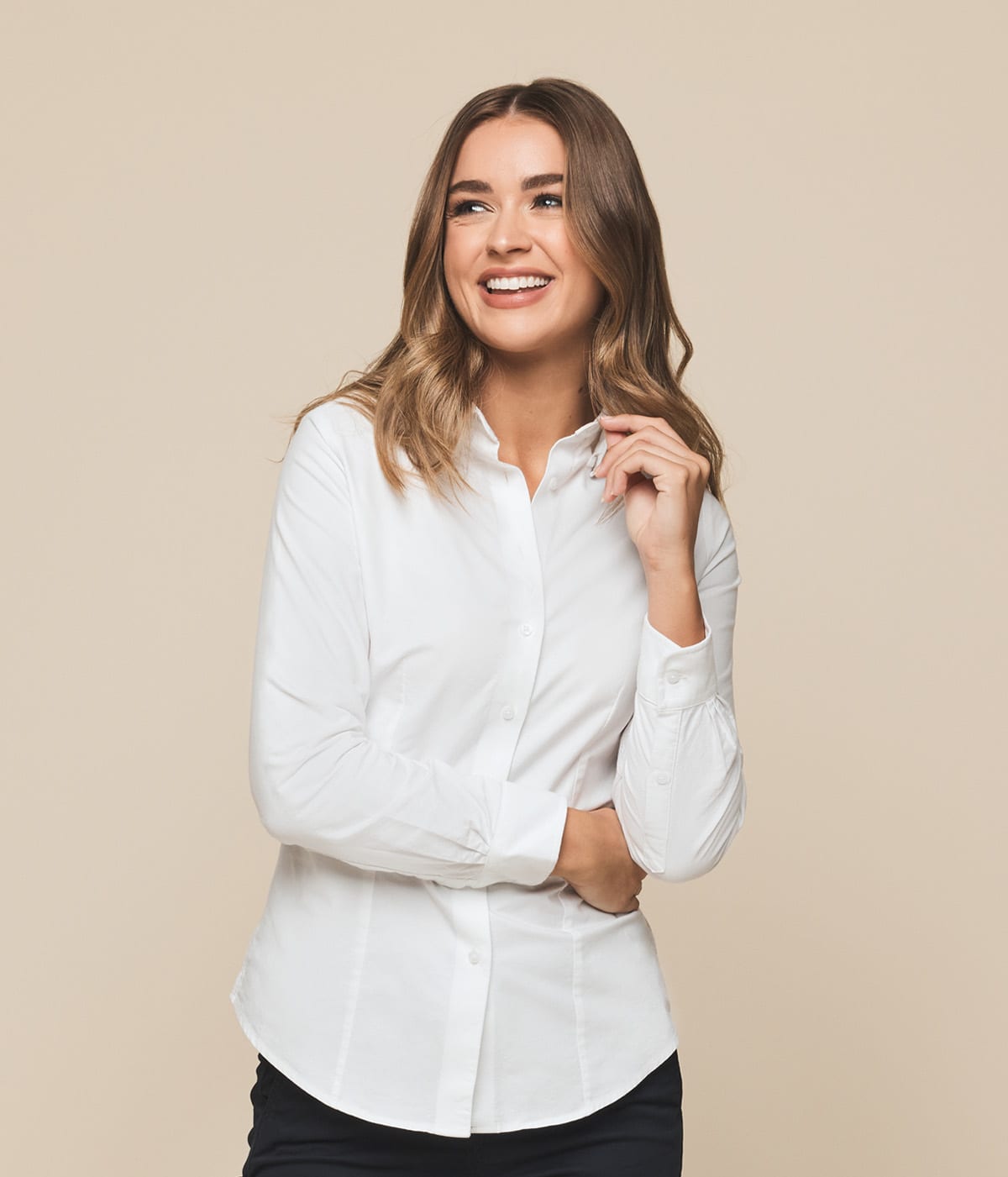 A woman in a white button-up shirt smiles, showcasing the Ashton Cotton Oxford Shirt. The shirt features a logo.