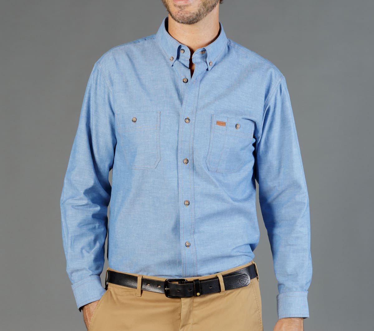 A light blue button-up work shirt featuring two chest pockets and a logo. The model wears it with beige trousers.