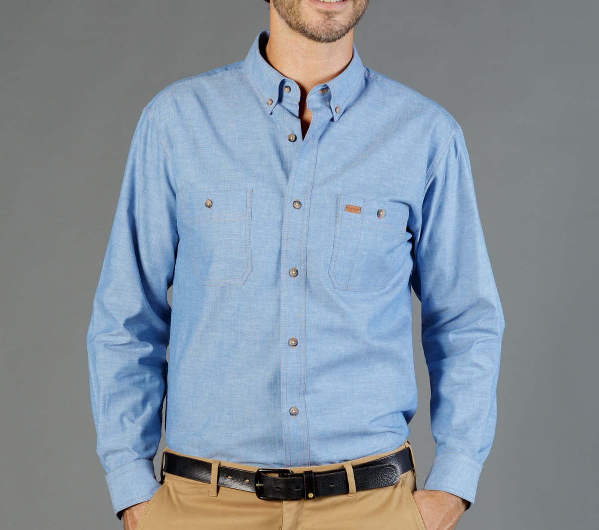 A blue long-sleeve work shirt featuring two chest pockets and a logo, set against a grey background.