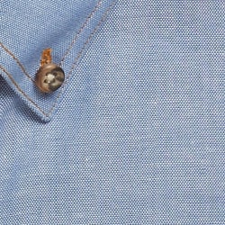 A blue work shirt featuring a buttoned collar and textured fabric. It has a logo on the side.