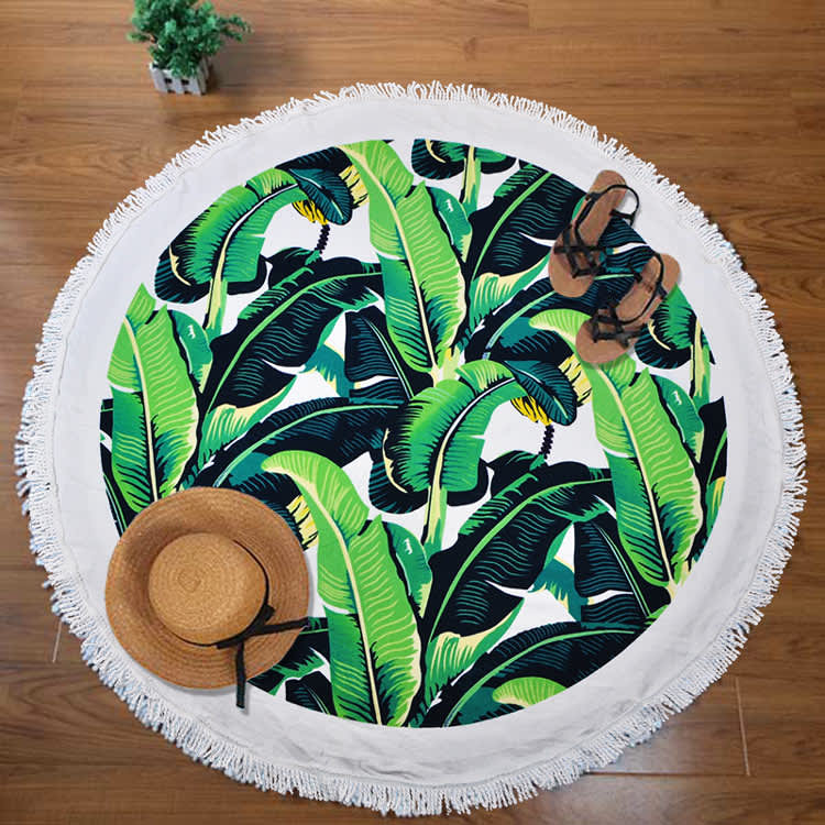 A round towel featuring a vibrant banana leaf design in green and dark green, with a fringed edge.
