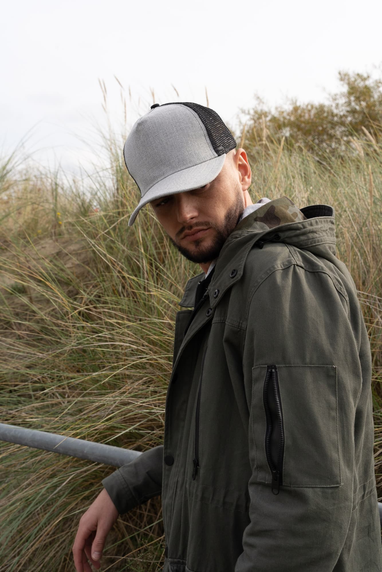 Grey Marle American Twill With Mesh Back HE-3821 A grey marle cap with a mesh back worn by a man in a green jacket, standing near grassy terrain.
