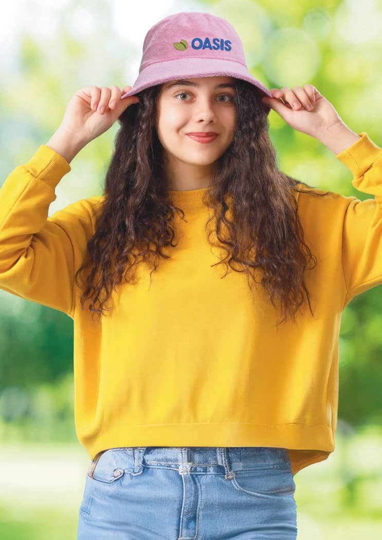 Terry Towelling Bucket Hat HE-3970 A pink terry towelling bucket hat with a logo, worn by a smiling person in a yellow sweatshirt against a green background.