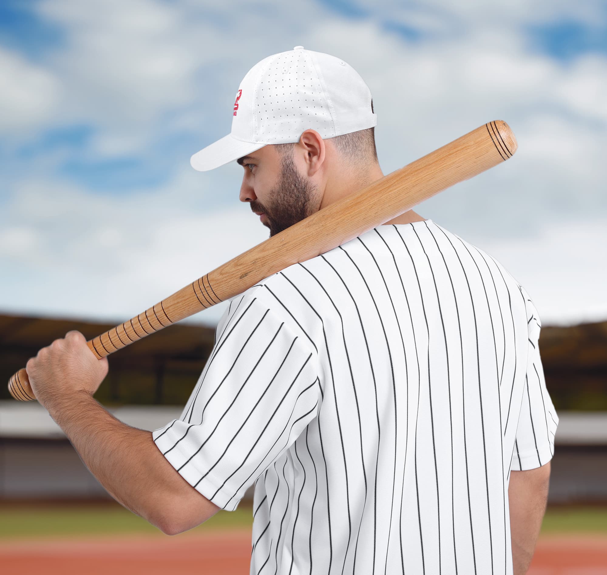 Breathable Poly Twill with circle perforations HE-3975 A man wearing a white cap with circle perforations and a striped baseball jersey holds a wooden bat over his shoulder.
