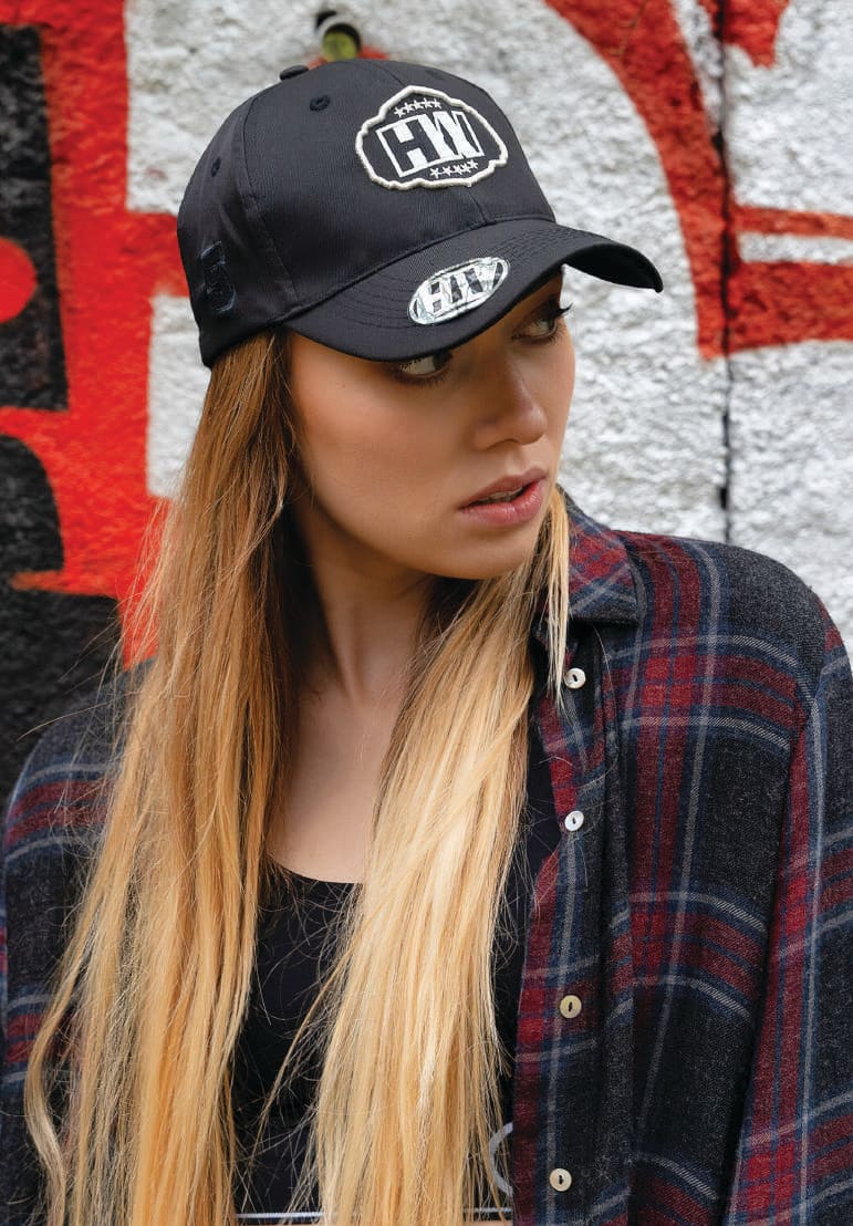 Premium American Recycled Twill Cap HE-3981 A black cap with a logo is worn by a model with long hair, against a graffiti backdrop.
