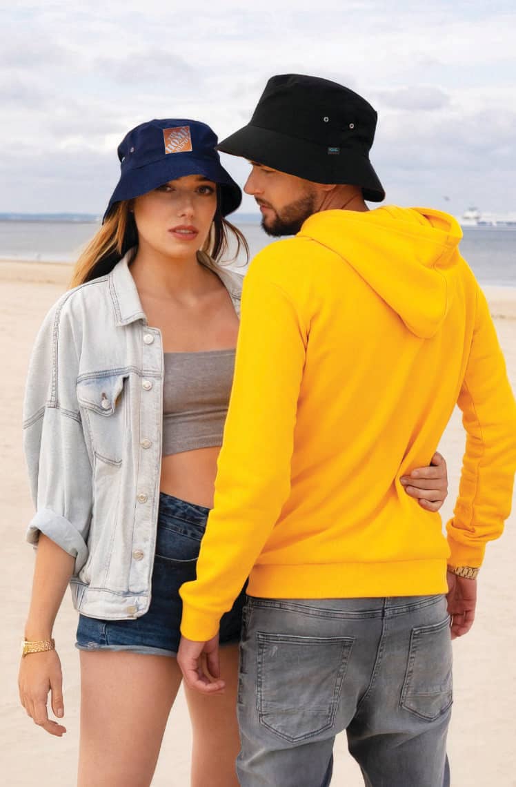 Recycled Breathable Poly twill Bucket Hat HE-3983 Two individuals on a beach, one wearing a navy bucket hat and the other in a black bucket hat, both casual outfits.