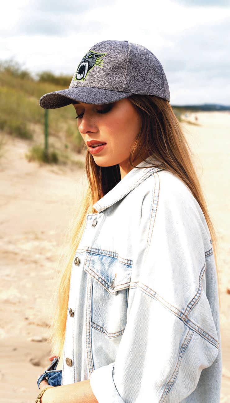 Cationic Sports Jersey HE-3998 A grey cap with a logo, worn by a woman with long hair, standing on a sandy beach.