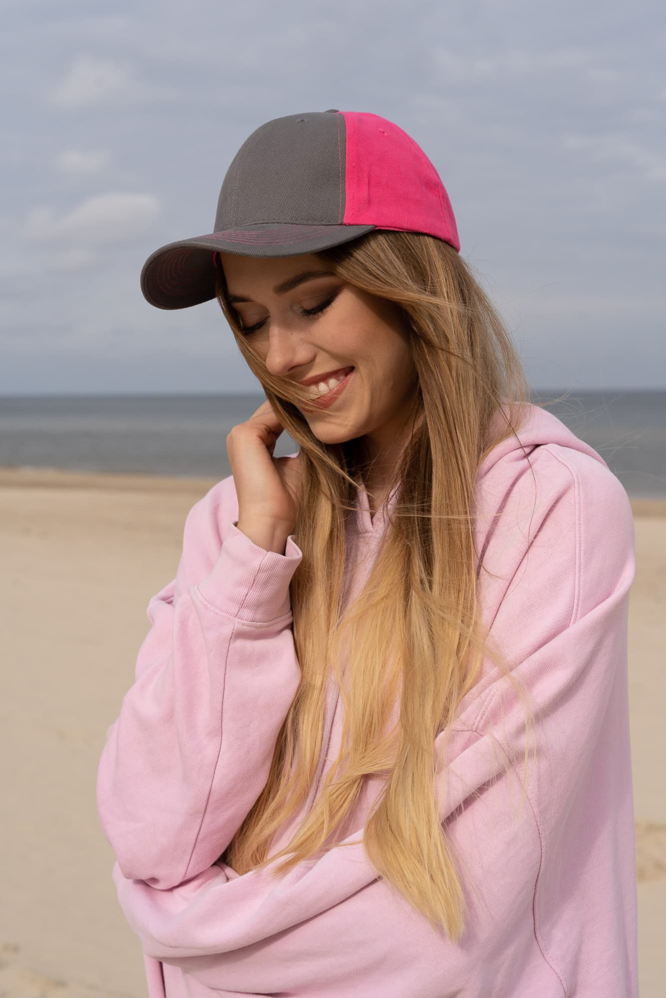 Brushed Heavy Cotton Contrast Cap HE-4001 A cap with a grey and pink design is worn by a woman smiling on a beach. The background features sand and sea.