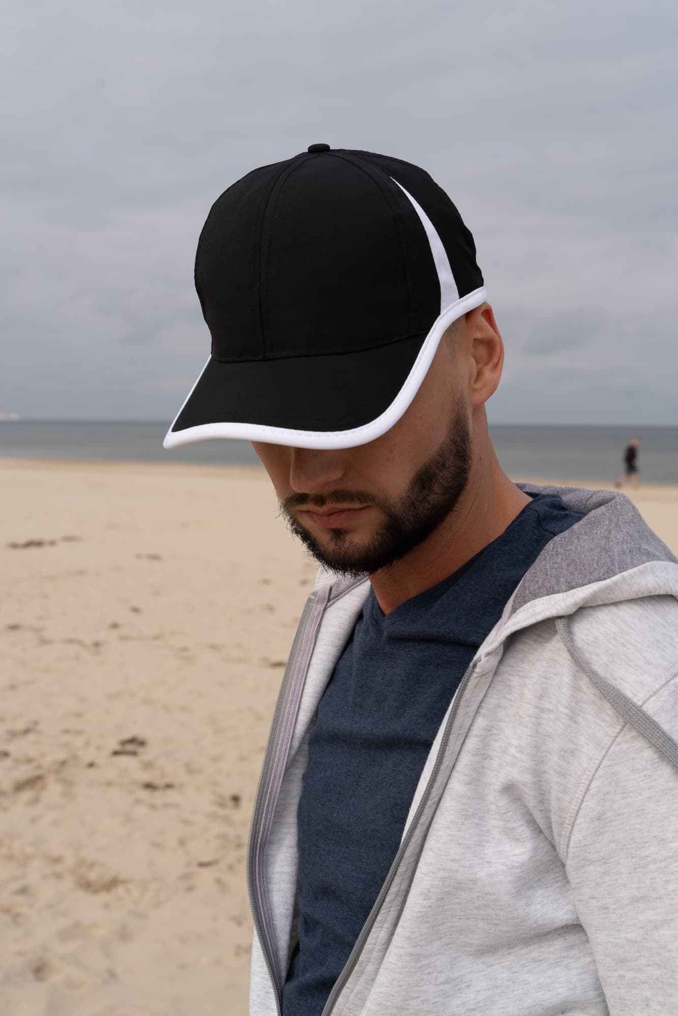 Sports Ripstop with Inserts and Trim HE-4004 A black cap with white trim, worn by a person at a beach, with a cloudy sky in the background.