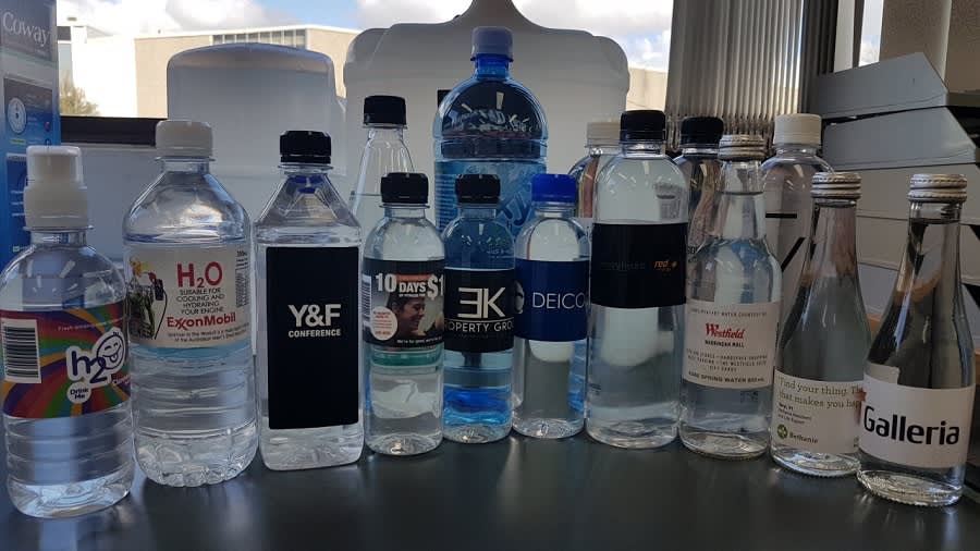 A drink bottle collection featuring various sizes and designs, including clear bottles, a blue bottle, and several with labels.