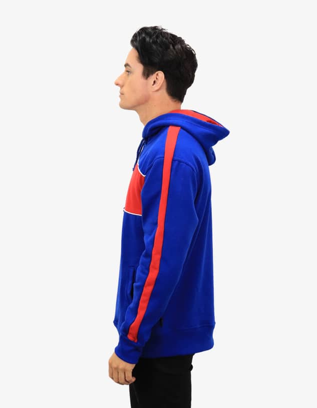 A blue hoodie with red stripes, featuring a hood and a logo. Side view of the garment worn by a model.