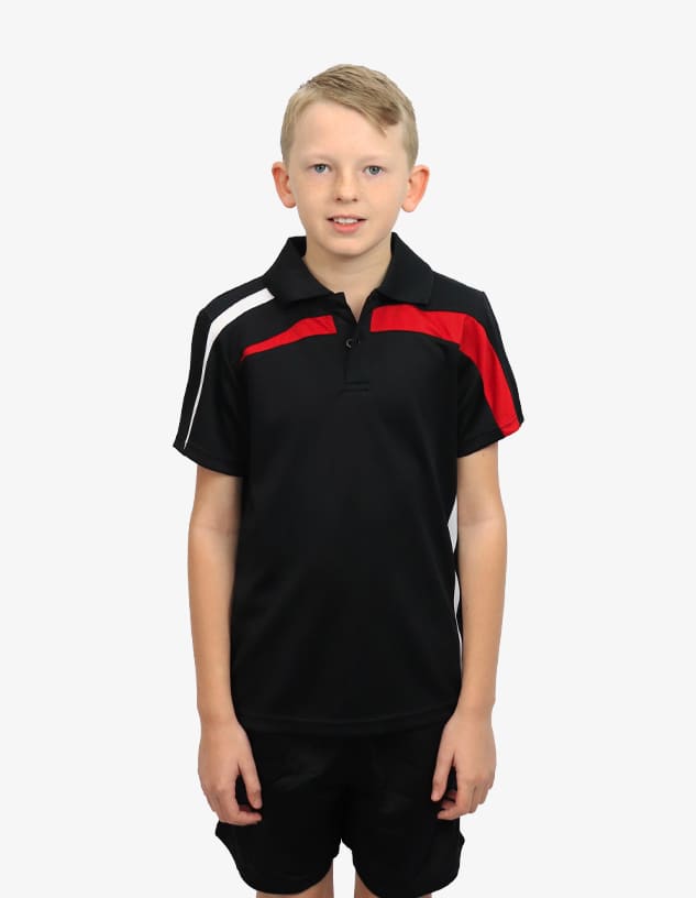 A boy stands wearing a black polo shirt with red and white accents, paired with black shorts. The shirt has a logo on it.
