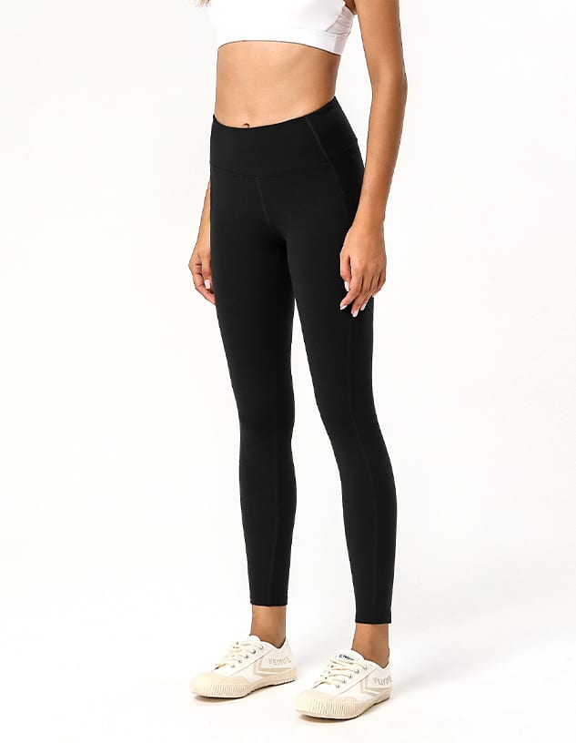 A pair of black leggings worn with a white crop top and white sneakers, featuring a logo on the waistband.