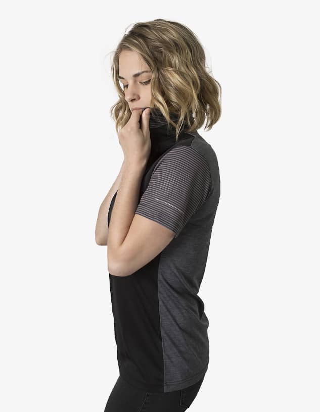 A polo shirt featuring a black and grey design, modelled by a person with wavy hair. The shirt has a logo.