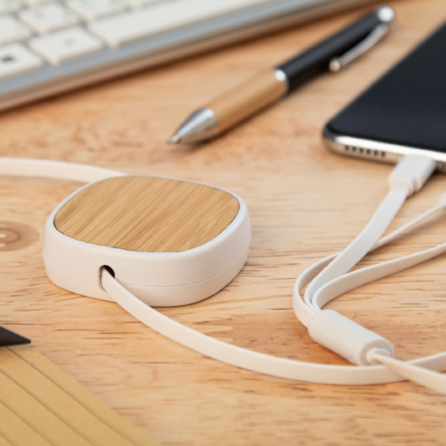 A USB charger cable with a bamboo and white casing, placed on a wooden surface alongside a pen and smartphone.