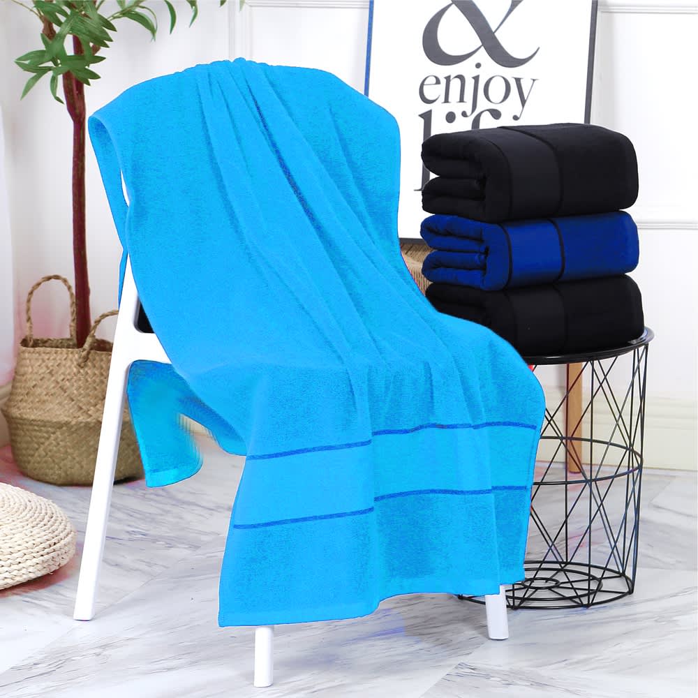 A bright blue bath towel draped over a white chair, with stacked black and blue towels beside it.