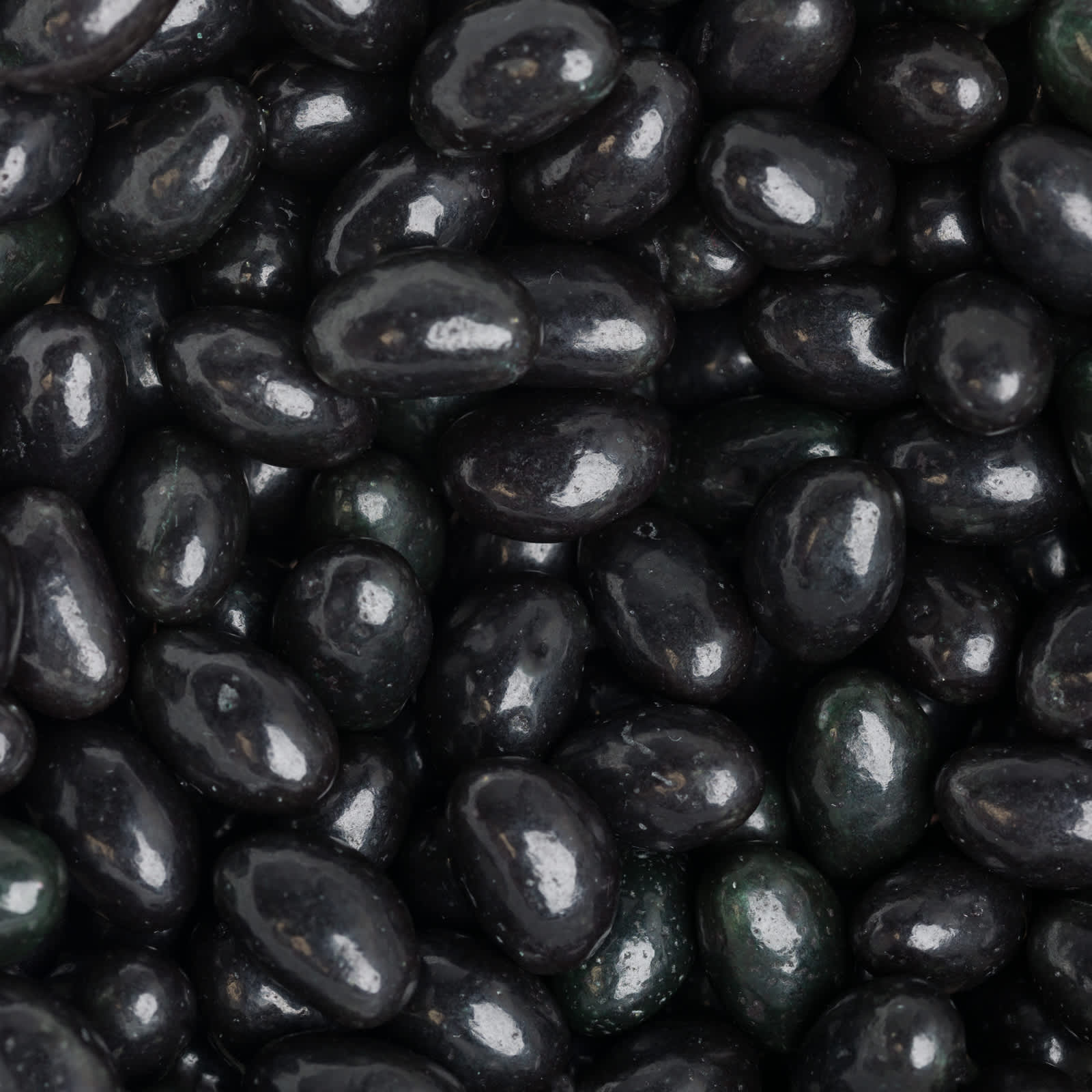 A close-up of shiny black jelly beans, showcasing their smooth, glossy surface and varied shapes.