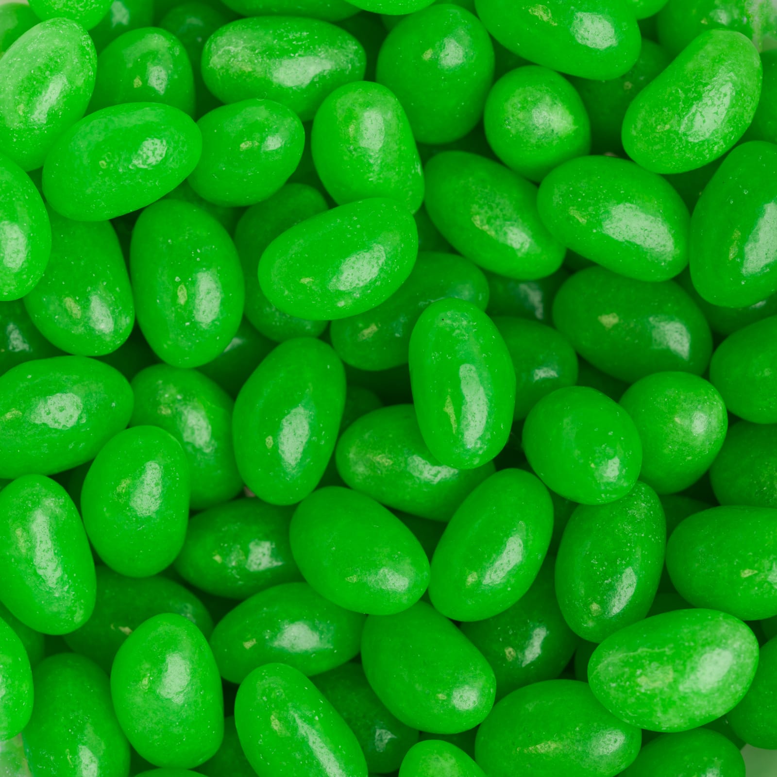 A close-up of shiny green mini jelly beans, displayed in abundance with a glossy surface.