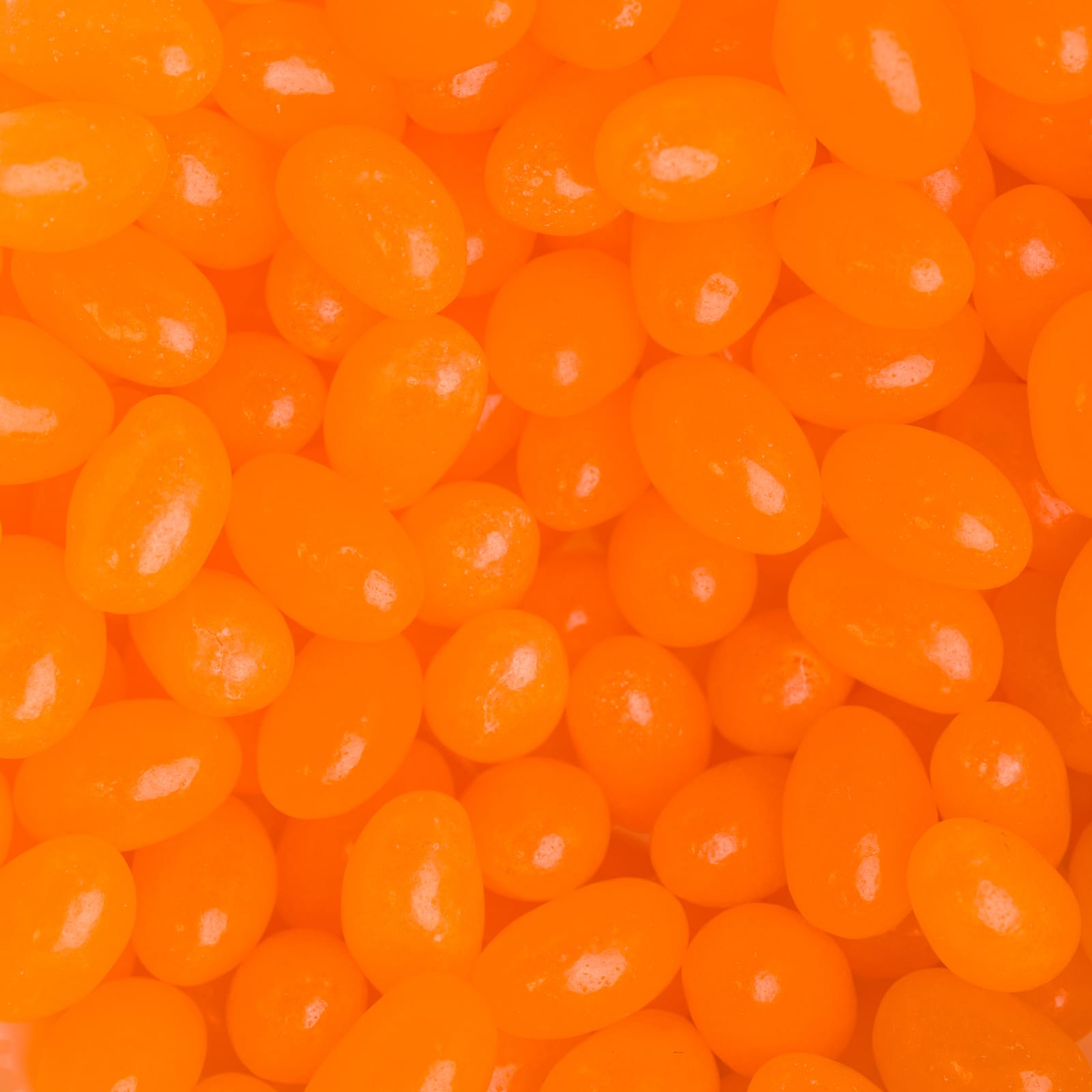 A close-up of bright orange jelly beans in various shapes and sizes, glossy and eye-catching in appearance.
