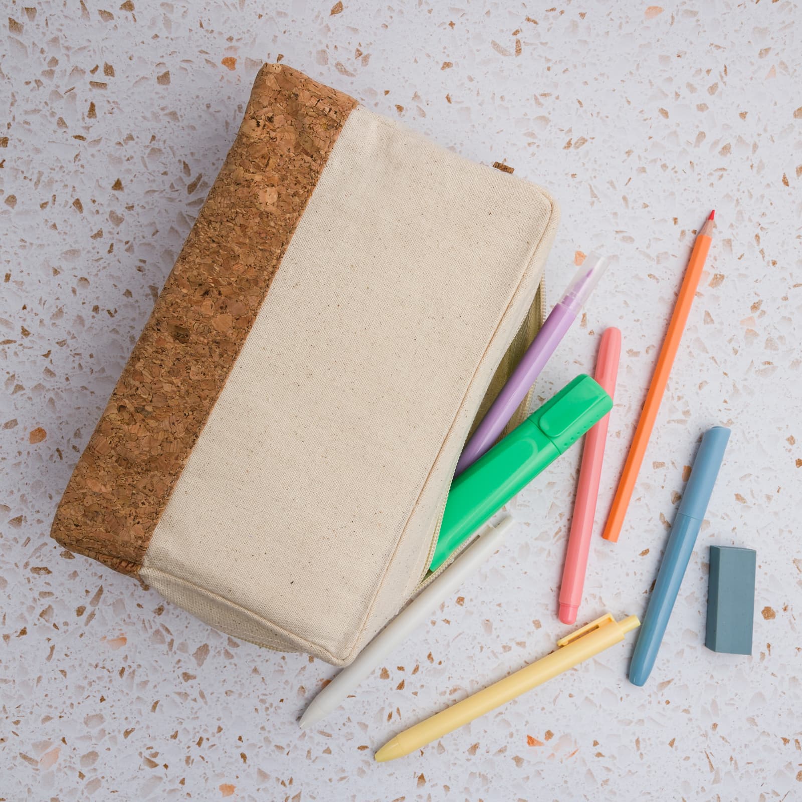 A utility case in cream and cork, with colourful pens and an eraser scattered beside it.