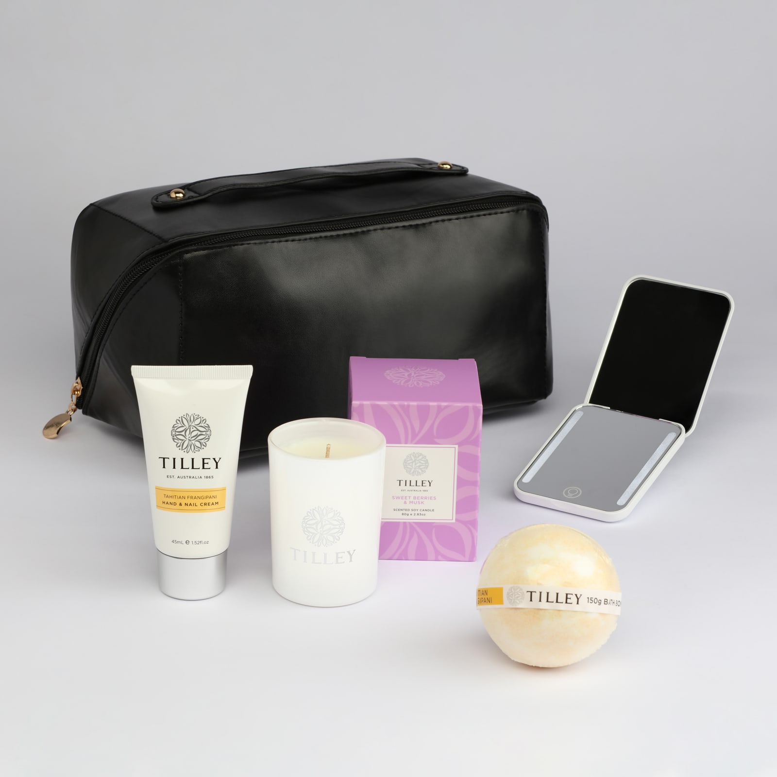 A black toiletry bag containing a tube of cream, a candle, a mirror, a bath bomb, and a boxed product.