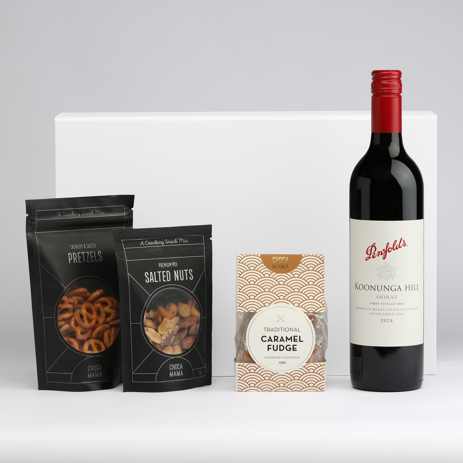A drink bottle of red wine accompanied by packets of salted nuts, pretzels, and caramel fudge. All items are elegantly arranged.