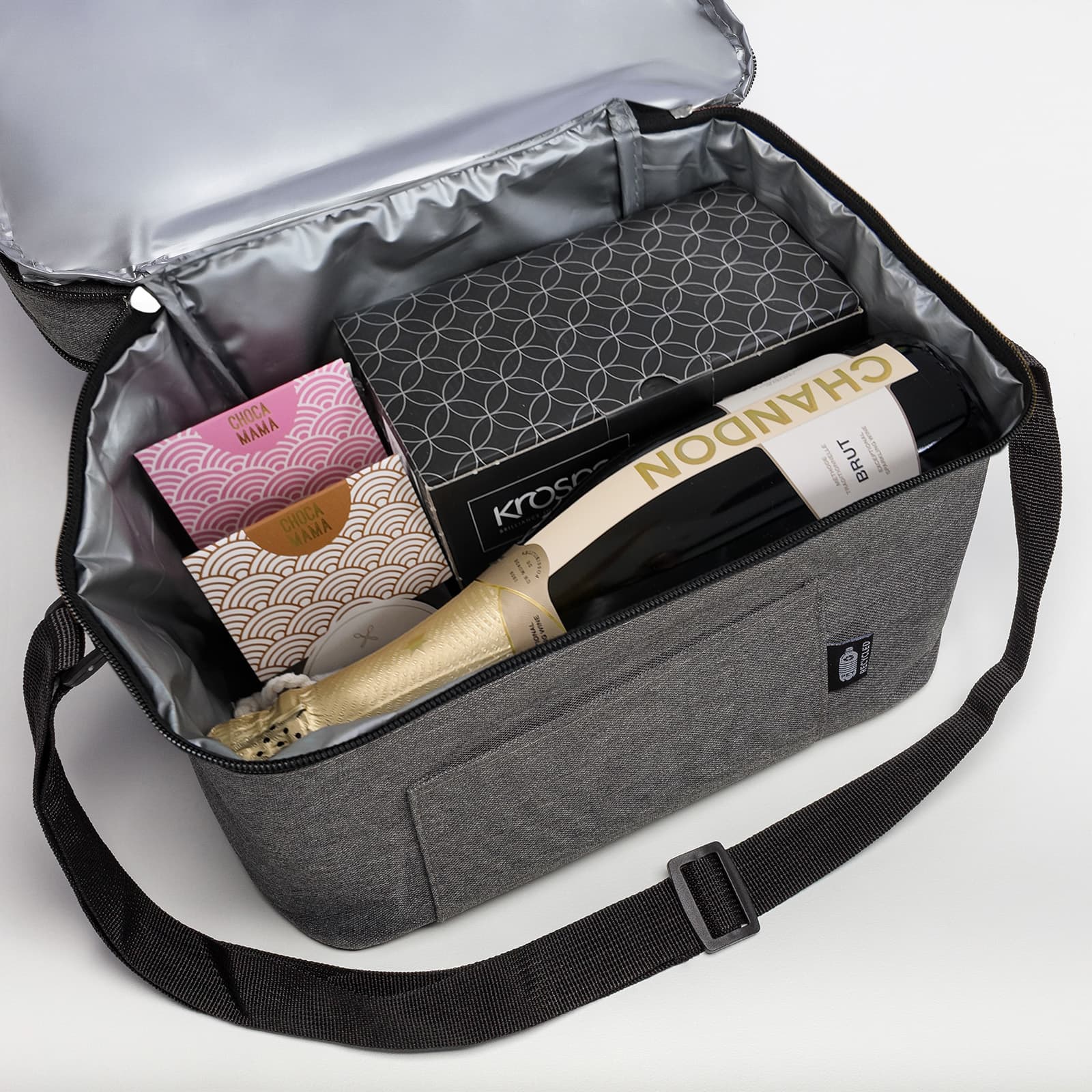 A drink bag in grey containing champagne, chocolates, and a box, with a silver insulated lining.