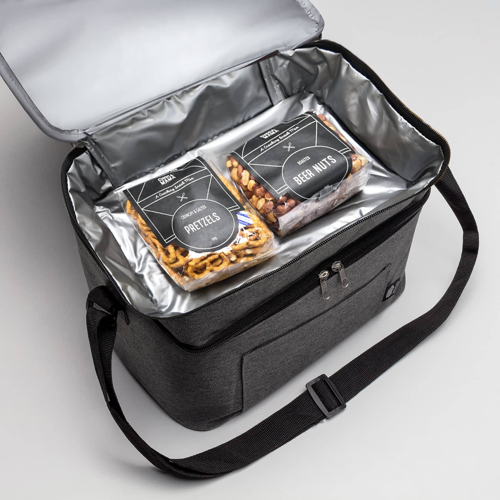 A grey insulated cooler bag with a zip, containing packages of pretzels and beer nuts inside.