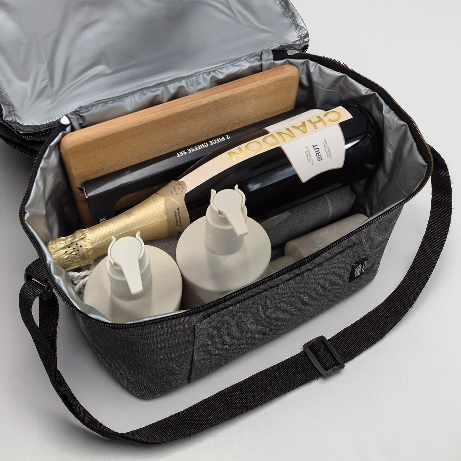 A grey cooler bag containing bottles of wine, skincare products, and a wooden board, all neatly organised inside.