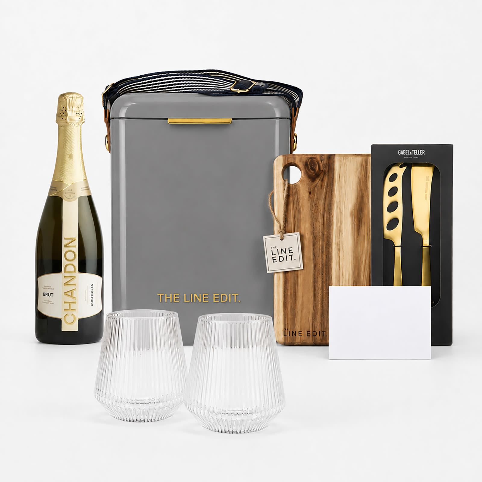 A grey insulated hamper containing a bottle of sparkling wine, two glass tumblers, a wooden cutting board, and a knife set.