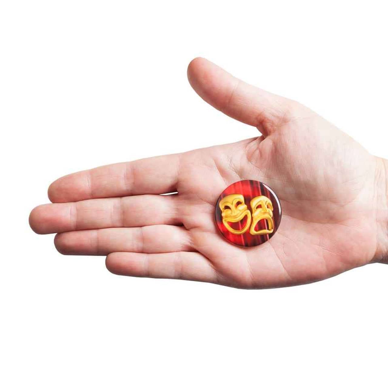 A hand holding a 38mm round badge featuring a design with theatrical masks against a red background.