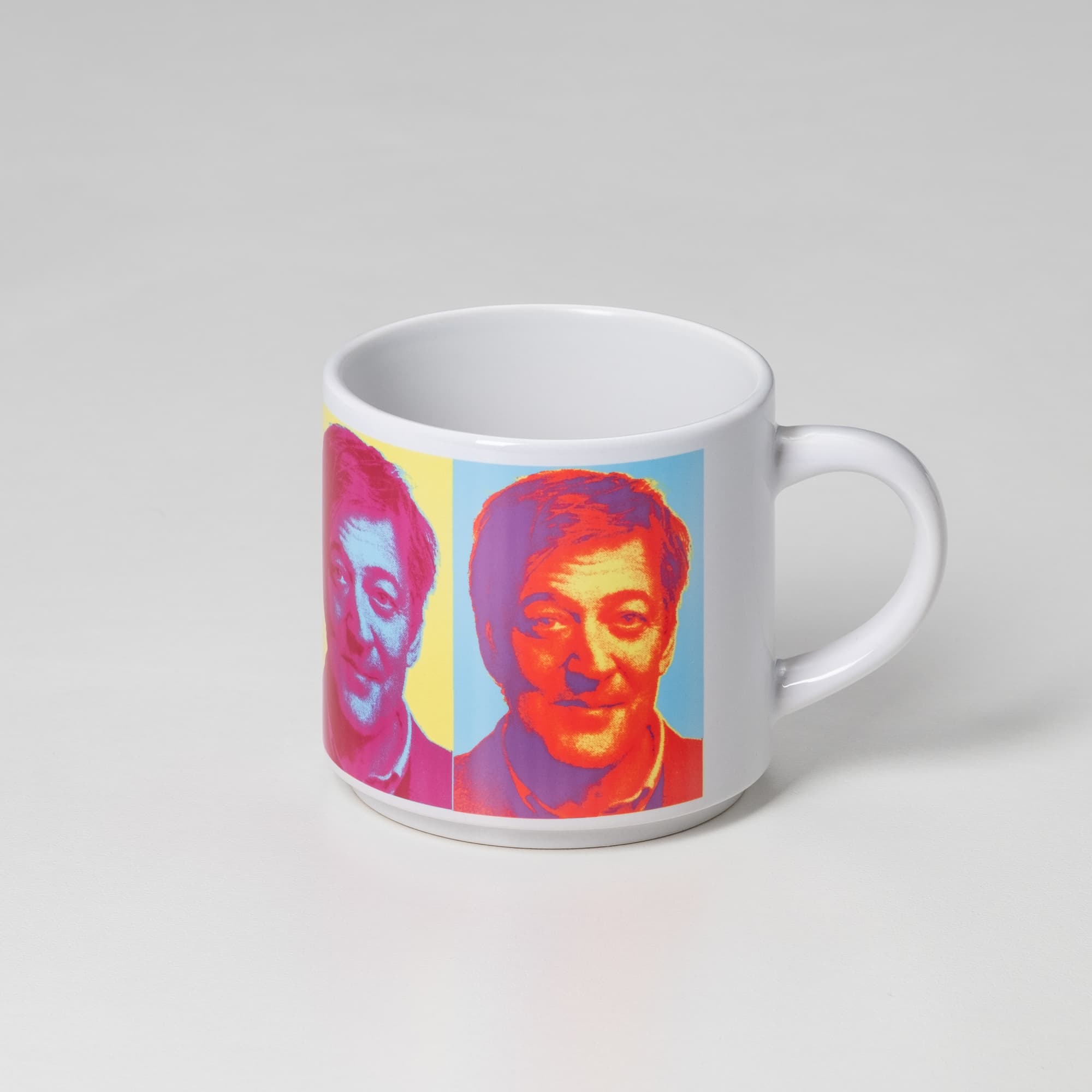 A coffee mug with a bright design featuring stylised portraits in pink and blue. The mug has a handle and a glossy finish.