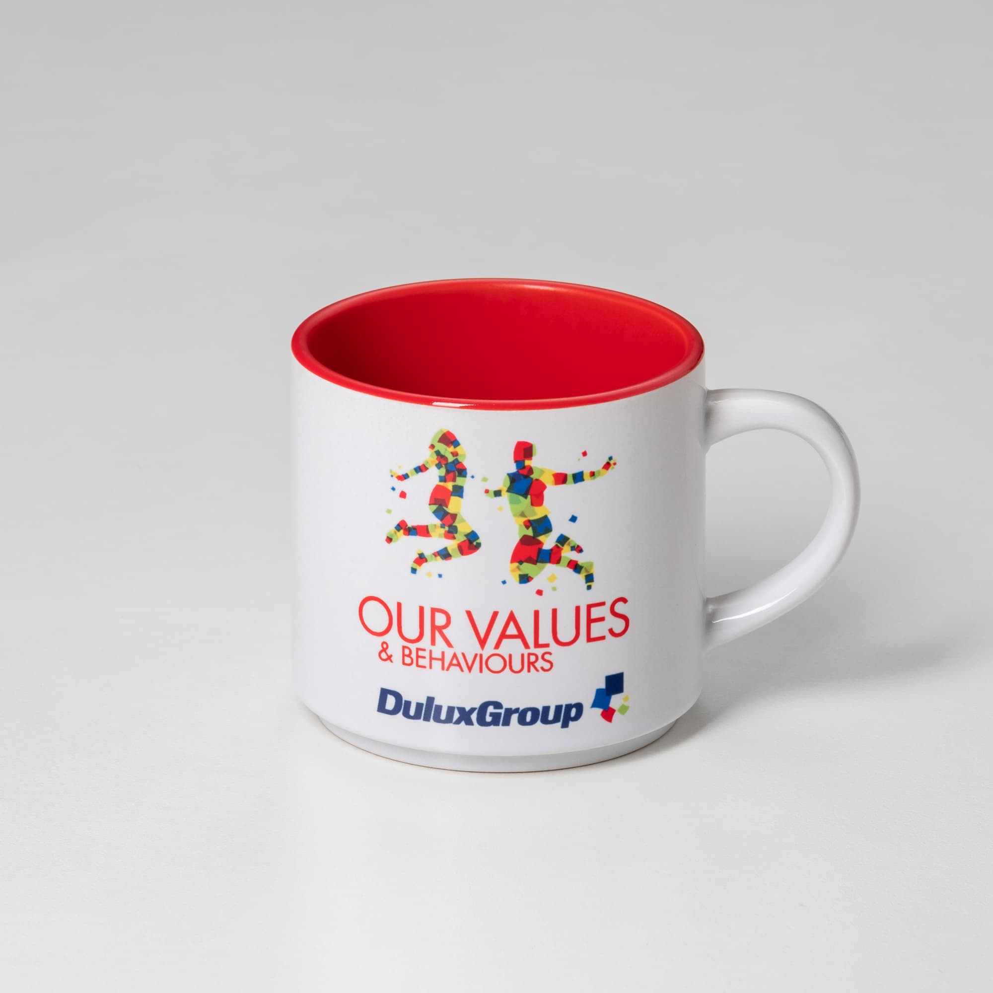 A coffee mug with a white exterior, red interior, and a logo featuring vibrant, colourful figures.