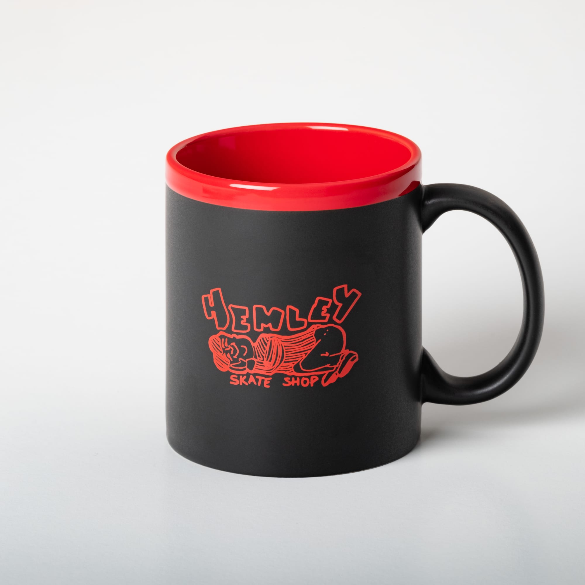 A coffee mug with a black exterior, red interior, and a logo featuring a skate shop design.