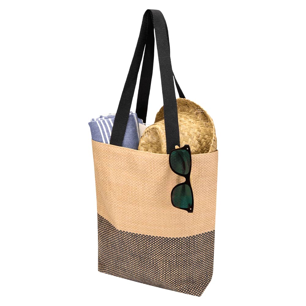 A beige and black tote bag with black straps, containing a towel and a straw hat, and sunglasses resting on the bag.