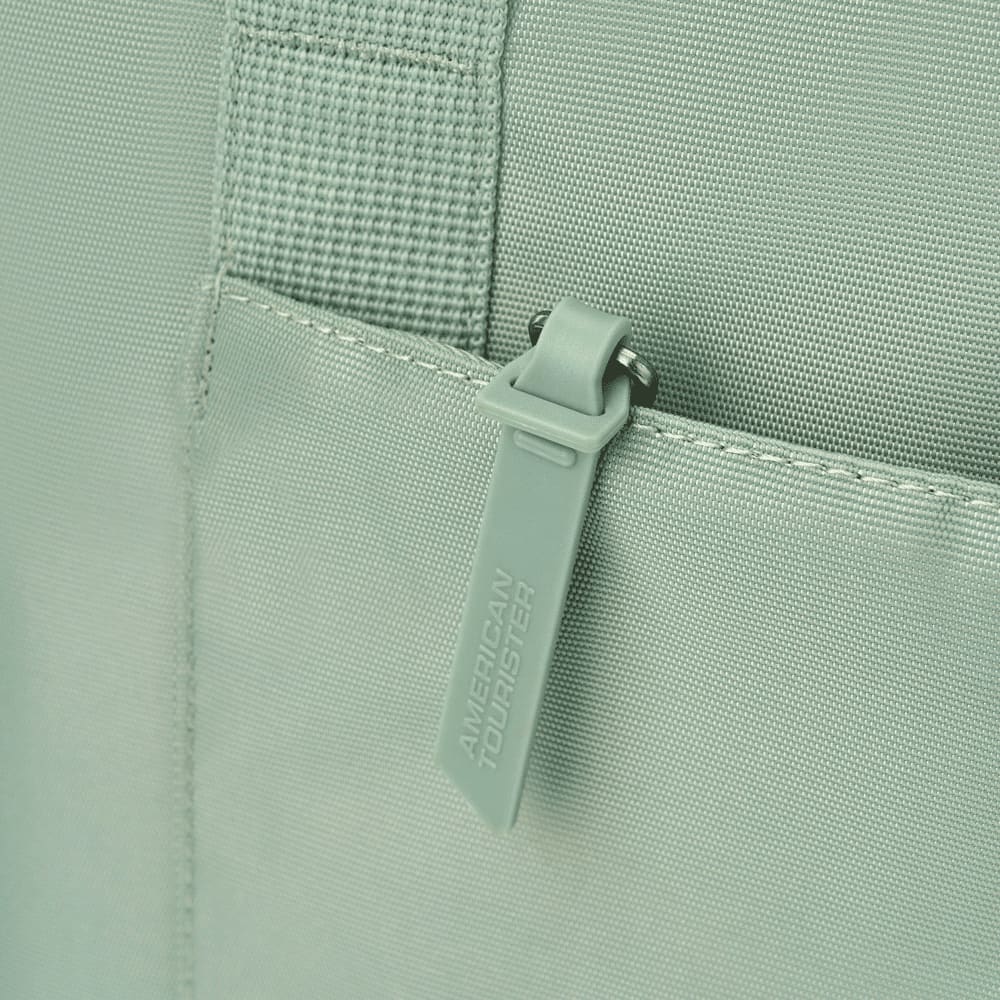 A mint green tote bag featuring a zippered pocket and textured fabric, with a logo on the zipper tag.