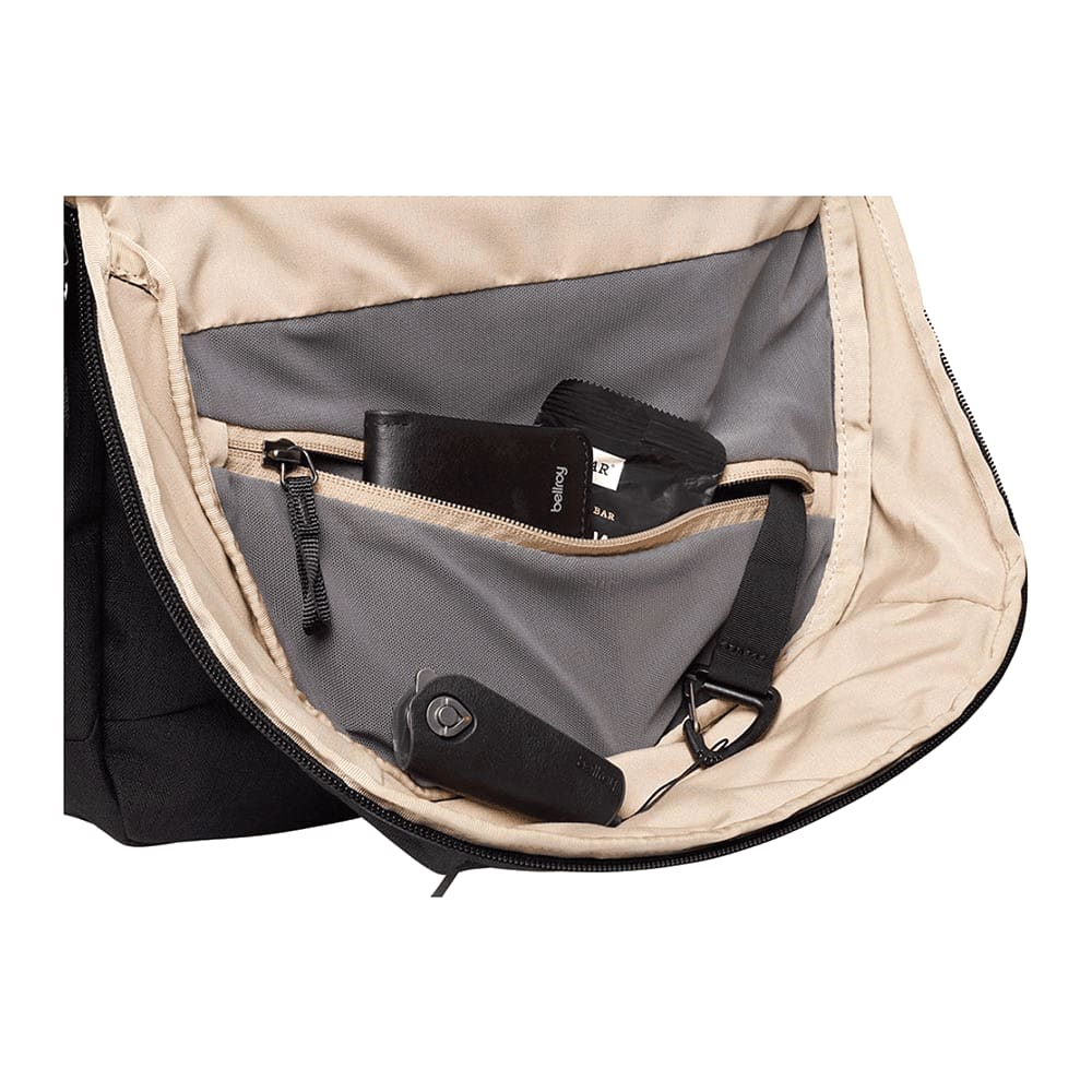 An open black backpack interior featuring a grey lining, small pockets, and various items like a wallet and a keychain.