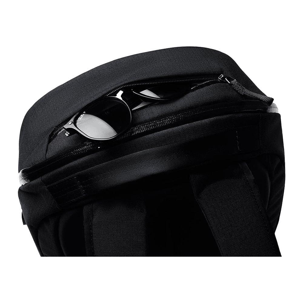 A black backpack with a zippered compartment, containing a pair of sunglasses. It features a logo on the exterior.
