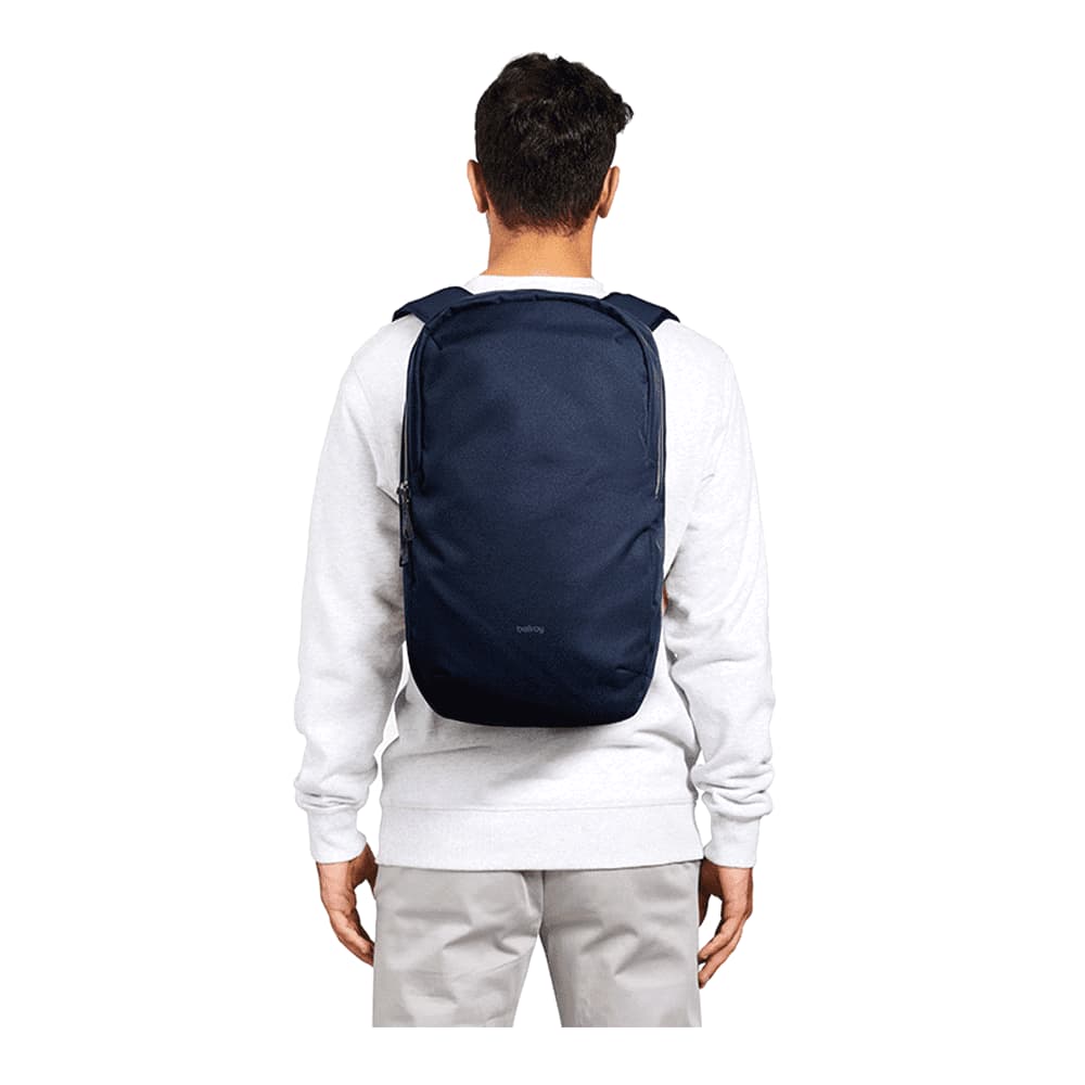 A person wearing a navy blue backpack, featuring padded shoulder straps and a simple design. The backpack has a logo.