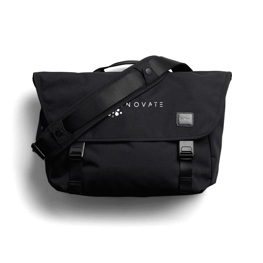 A black satchel bag with a shoulder strap and a logo, featuring front clasps and a flap cover.
