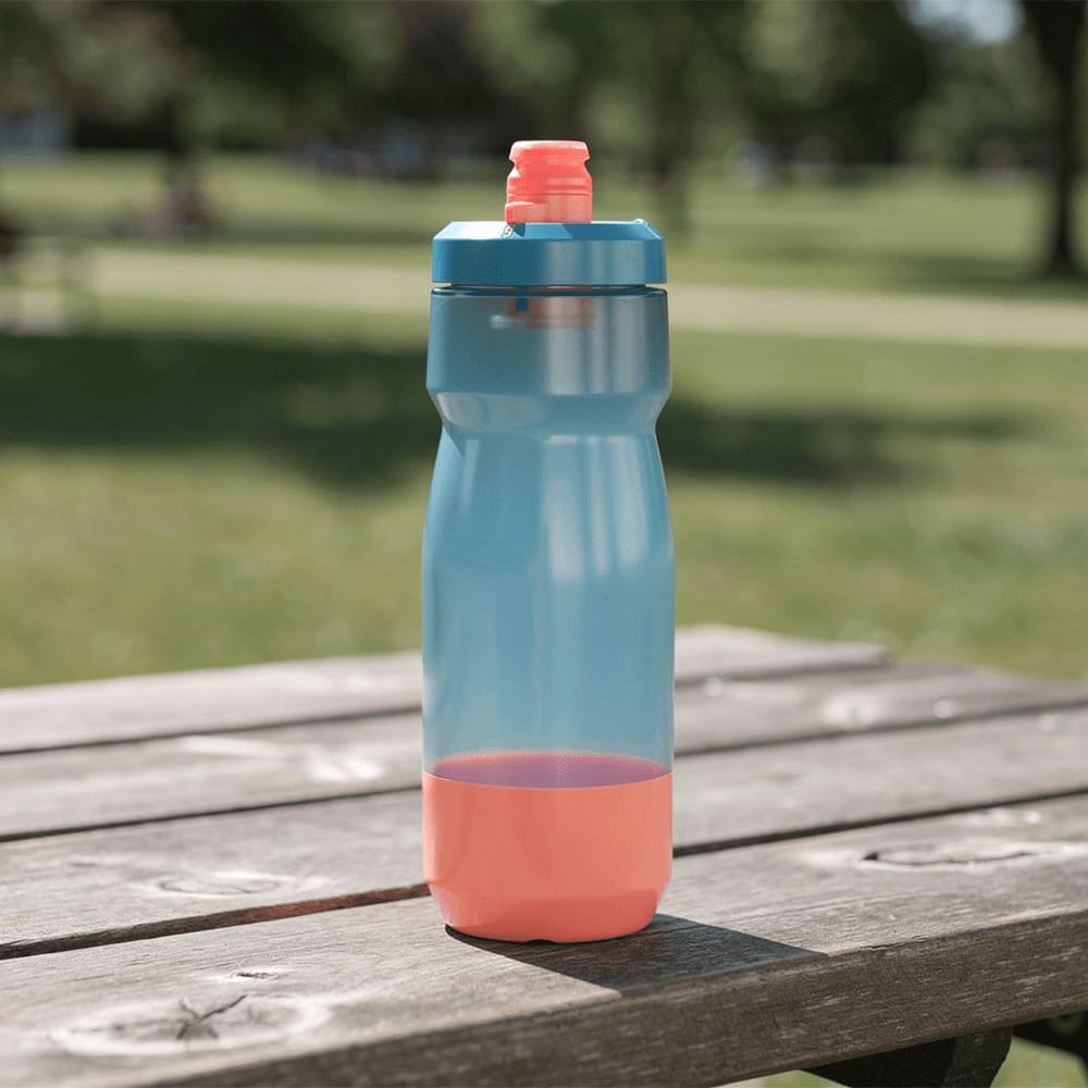 A drink bottle in blue and coral, featuring a screw-top lid and a curved design, resting on a wooden table outdoors.